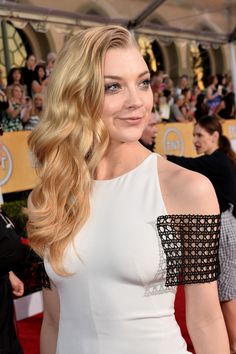 a woman with long blonde hair wearing a white dress and posing for the camera at an event