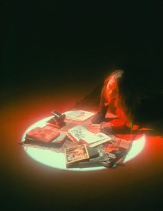 a woman sitting on the floor surrounded by books and magazines in front of her face