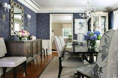 a dining room with blue wallpaper and white chairs in front of a glass table