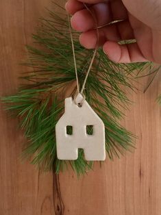 a hand holding a white ceramic house ornament with pine needles on the side