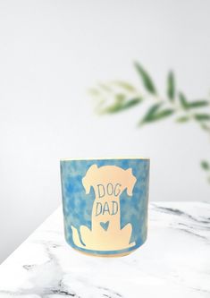 a blue and white dog mug sitting on top of a marble table next to a potted plant