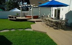 a deck with chairs and an umbrella in the middle of a lawn area next to a house