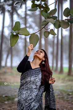 a woman standing under a tree with her hands in the air and looking up at leaves