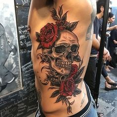 a man with a skull and roses tattoo on his back is standing in front of a wall