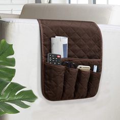 a white couch with a brown pocket for cell phones and remotes in it next to a potted plant