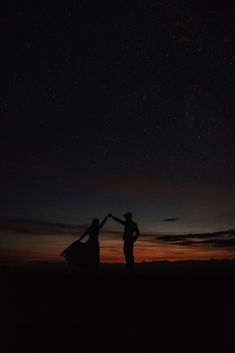 two people standing in the dark with their arms around each other as the sun sets