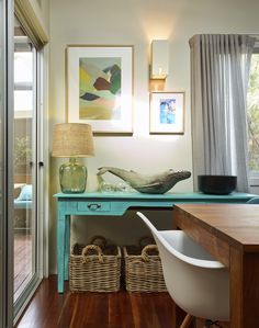 a blue desk with baskets underneath it and pictures on the wall behind it, along with two lamps