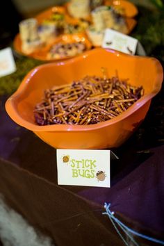 an orange bowl filled with sticks sitting on top of a purple cloth covered tablecloth