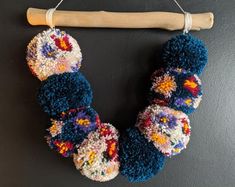 a multicolored beaded necklace hanging from a wooden stick on a black wall