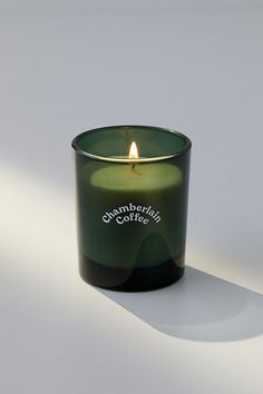 a green candle sitting on top of a white table next to a black cup filled with coffee