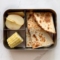 a metal container filled with food on top of a white table next to an apple