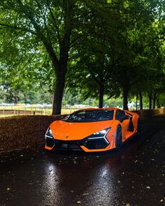 an orange sports car driving down a wet road