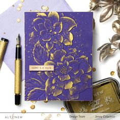 a purple card with gold foil flowers on it next to some ink pens and other items