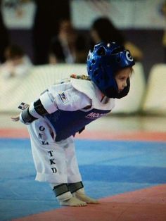 a young child wearing a blue helmet and white uniform is standing on one leg with his hands in the air