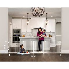 a woman standing next to a baby in a kitchen with an adult and child sitting on the floor