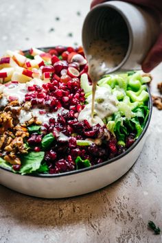 a person pouring dressing into a salad in a bowl