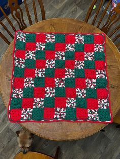 a table with a red and green blanket on it next to a brown chair in front of a wooden table