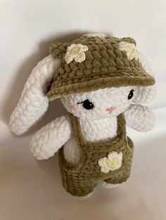 a white stuffed animal wearing a green hat and vest with flowers on it's chest