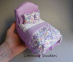 a hand is holding a miniature bed made out of cloths and fabric material with flowers on it