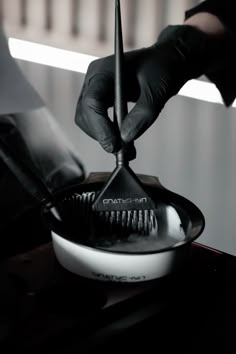 a person in black gloves holding a brush over a frying pan