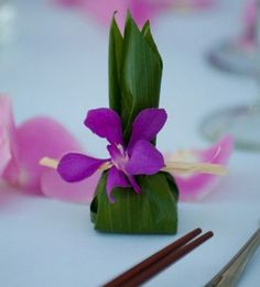 a purple flower sits on top of a table with chopsticks and wine glasses