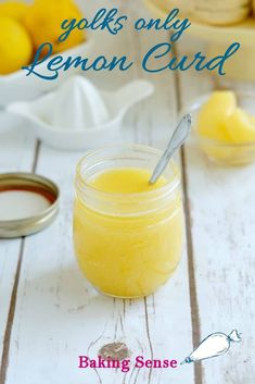 a jar filled with lemon curd sitting on top of a white wooden table next to a bowl of lemons