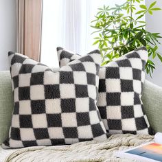 two black and white pillows sitting on top of a couch next to a plant in front of a window