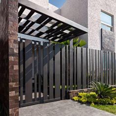 a modern gate in front of a house with plants and flowers on the side walk