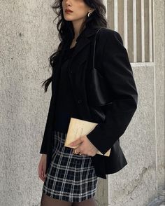 a woman standing in front of a building wearing a black blazer and plaid skirt