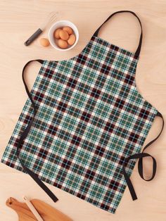 an apron with a plaid pattern on it next to wooden spoons, eggs and utensils