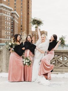 four bridesmaids in pink dresses and fur stoles pose for the camera with their bouquets