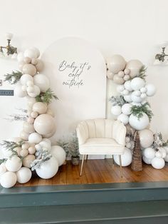 white balloons and greenery are on display in front of a fireplace mantel for a baby's first christmas party