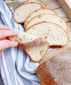 a person holding a piece of bread in front of some sliced bread on a wooden tray