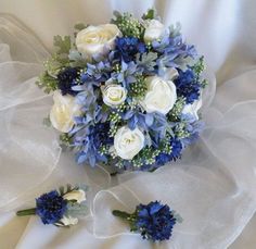 a bridal bouquet with white roses and blue flowers on a bed sheet in the sunlight