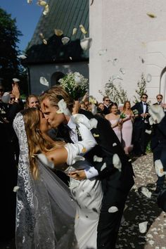 a bride and groom are kissing in front of a group of people who are throwing confetti into the air