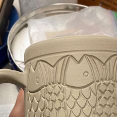 a close up of a person holding a cup with fish carvings on the bottom and sides