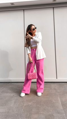 a woman standing in front of a wall wearing pink pants and a white blazer