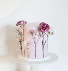 a white cake with flowers painted on the top and bottom, sitting on a stand