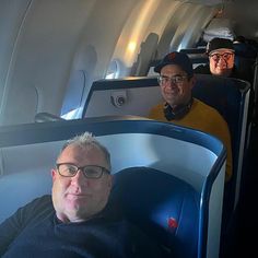 three men are sitting on an airplane with their heads turned to the side and looking at the camera