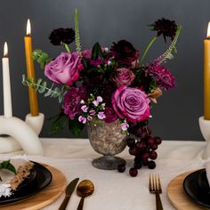 the table is set with black plates, silverware and purple flowers in a vase