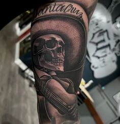 a man's arm with a skull wearing a cowboy hat and holding a guitar