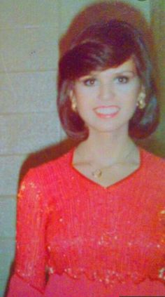 an old photo of a young woman in red sweater and gold earrings smiling at the camera