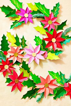 paper poinsettis and holly leaves are arranged on a beige surface with green, red, yellow, and pink flowers