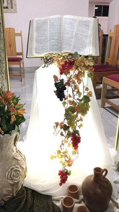 an open book is sitting on a table next to vases with flowers and leaves