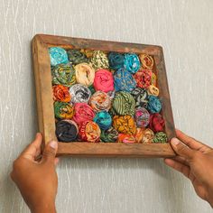 two hands holding a wooden box filled with different colored scarves on a white wall