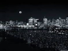 black and white photograph of city skyline at night with moon in sky over water,