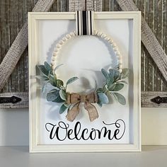 a welcome sign hanging from the side of a door with a wreath and ribbon around it