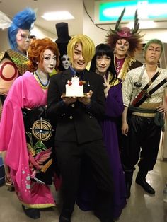 a group of people dressed up in costume posing for a photo with one holding a cake