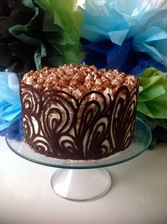 a cake with chocolate frosting and decorative swirls on top sitting on a glass plate