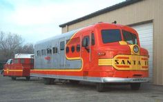 an orange and silver train parked in front of a building next to two red trucks